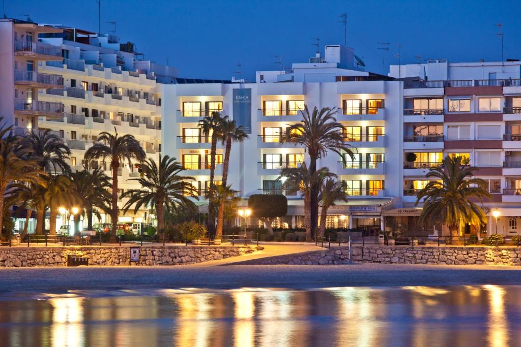 un edificio en la playa con palmeras delante en Apartamentos Bahia en Santa Eulalia del Río