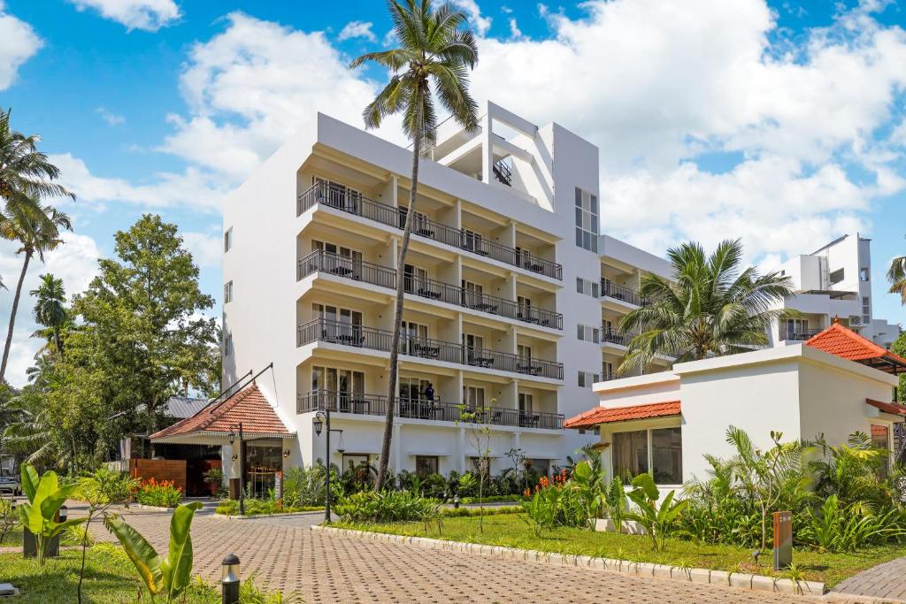 Club Mahindra Arookutty, Alleppey في Alleppey: مبنى ابيض امامه اشجار النخيل