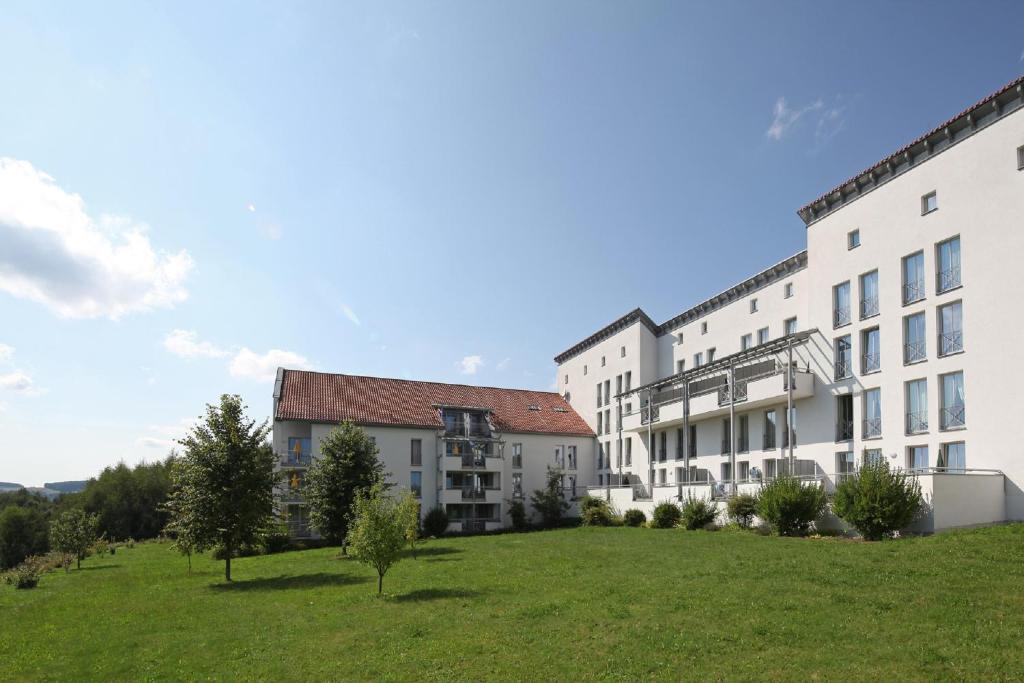 un groupe de bâtiments avec un champ herbeux devant dans l'établissement Appartement-Hotel Sibyllenbad, à Neualbenreuth