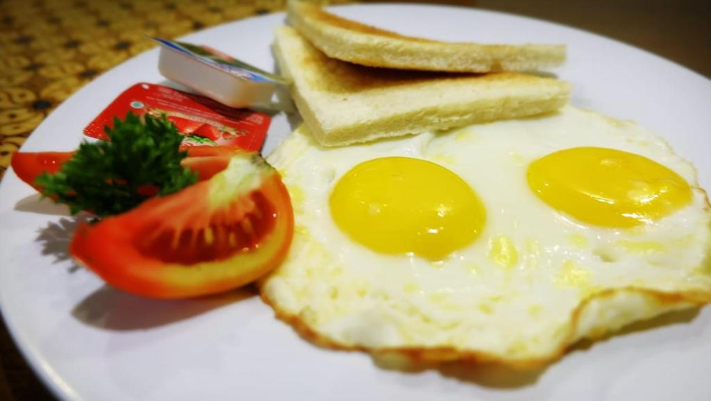 a white plate with eggs and toast and a tomato at Alia Home in Sanur
