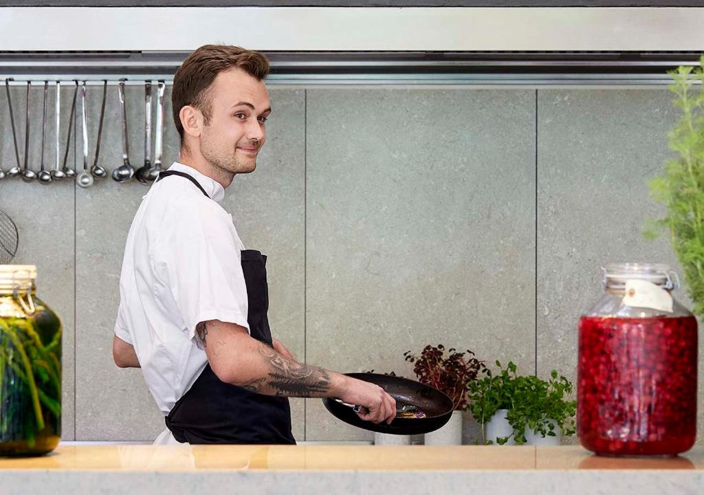 a man with a tattoo on his arm holding a plate in a kitchen at Charlottehaven in Copenhagen
