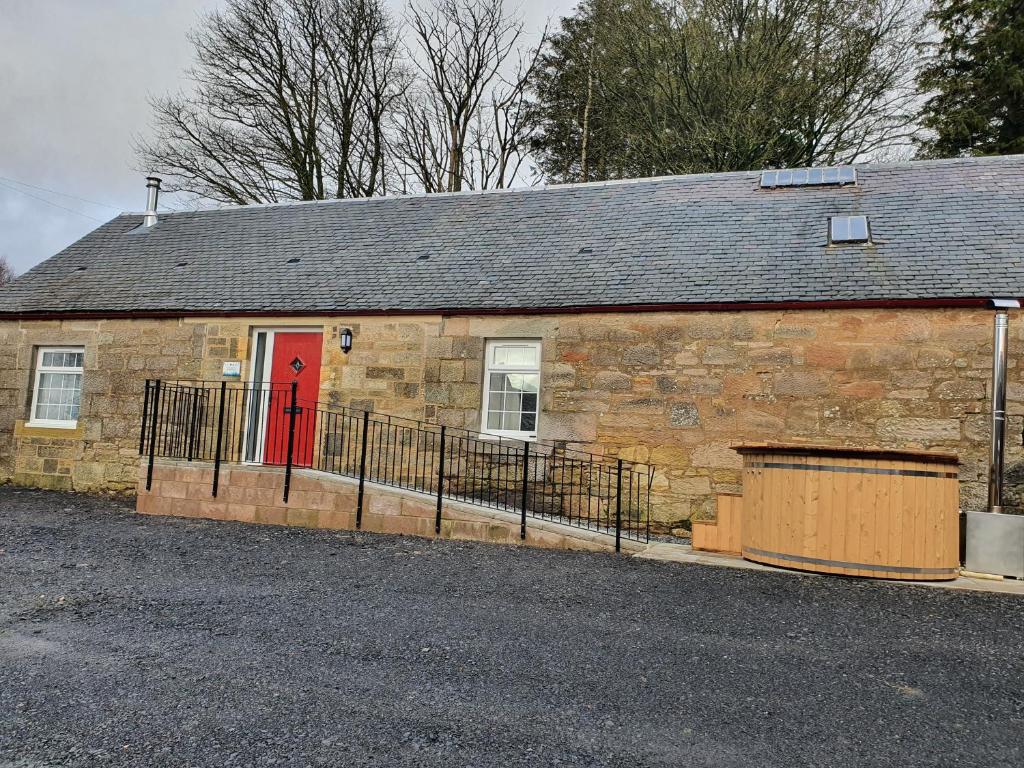 un edificio de ladrillo con una puerta roja en una calle en Inviting 2-Bed Barn with hot tub near Muirkirk, en Cumnock