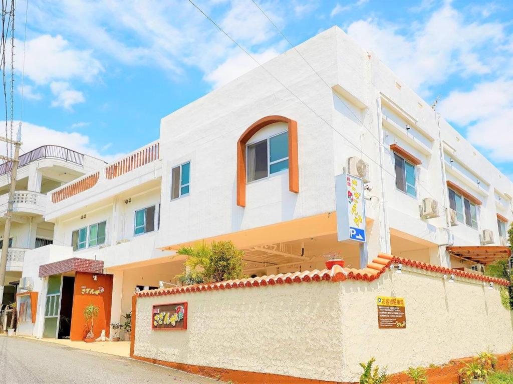 un edificio blanco con ventanas de color naranja en una calle en 民宿さざんか, en Okinawa City