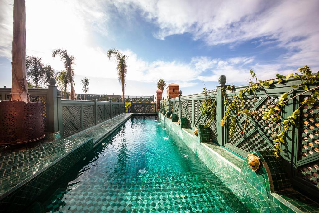 una piscina con agua azul y palmeras en Elegancia Riad Boutique & SPA en Marrakech