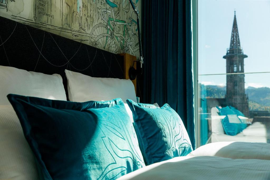 a bed with blue and white pillows next to a window at Motel One Freiburg in Freiburg im Breisgau