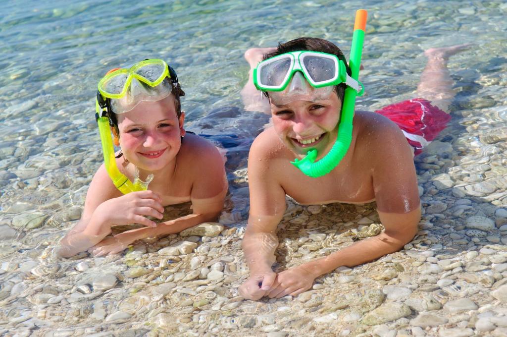 two people laying on the beach in the water at Valamar Diamant Hotel in Poreč