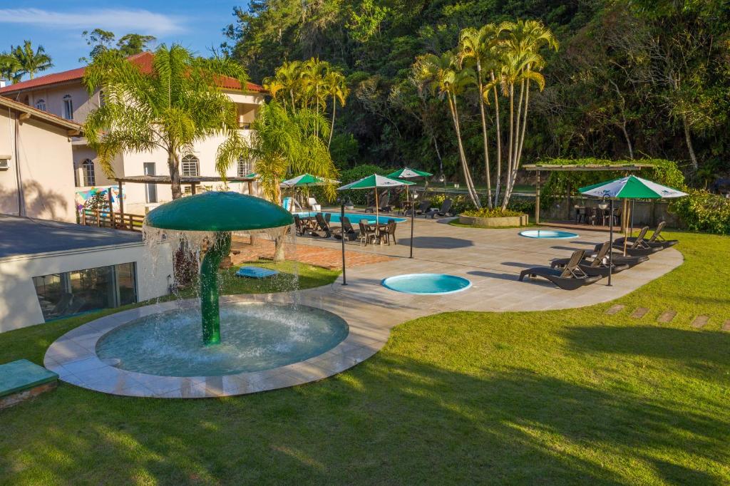 un parque con una fuente, mesas y sombrillas en Hotel Sandrini, en Tubarão