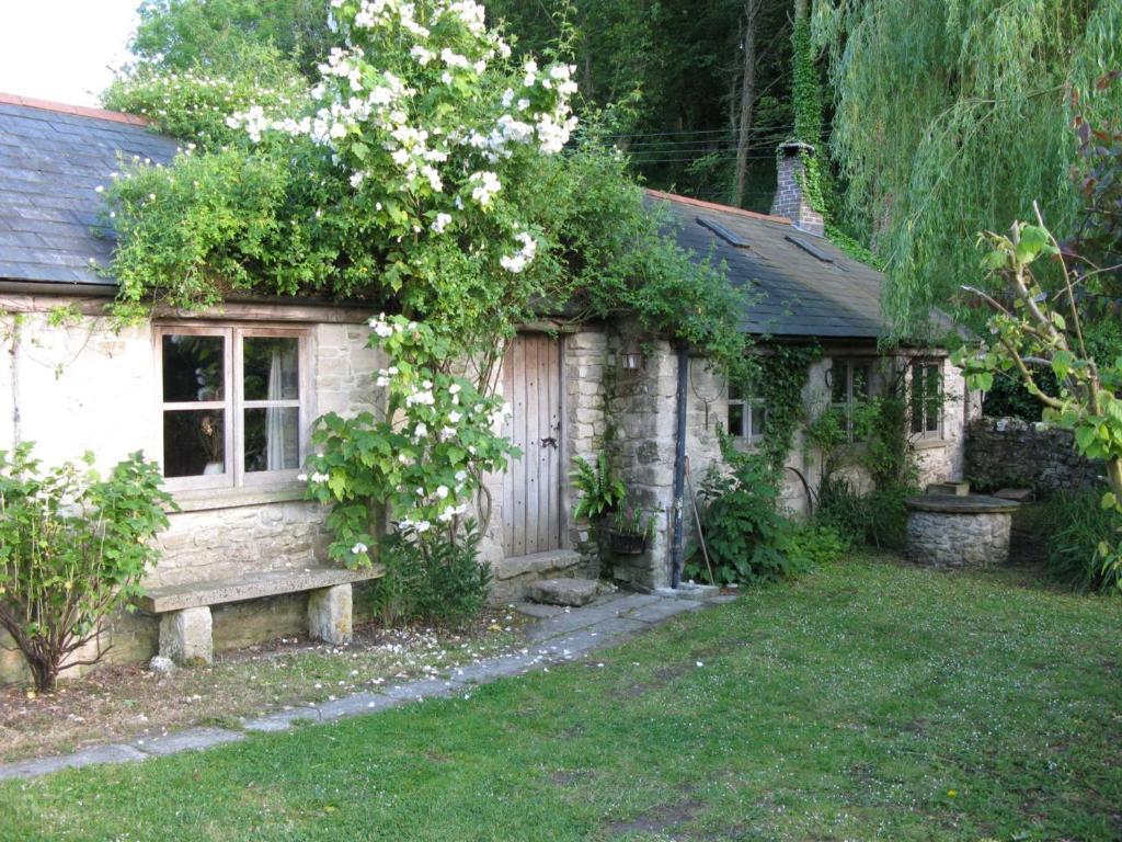 una pequeña casa de piedra con un banco en el patio en The Cartshed, en Osmington