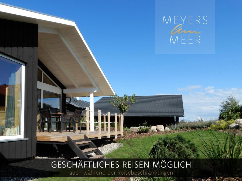 une maison avec une terrasse couverte et une terrasse avec des chaises dans l'établissement Schwarzes Holzferienhaus mit Sauna -- GARTENGLÜCK -- an der Ostsee, Zierow bei Wismar, Strand 500m, 2 Schlafzimmer, à Zierow