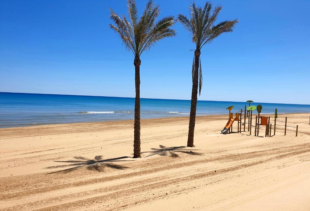 dos palmeras y un parque infantil en la playa en Apartamento Porticada, en Guardamar del Segura