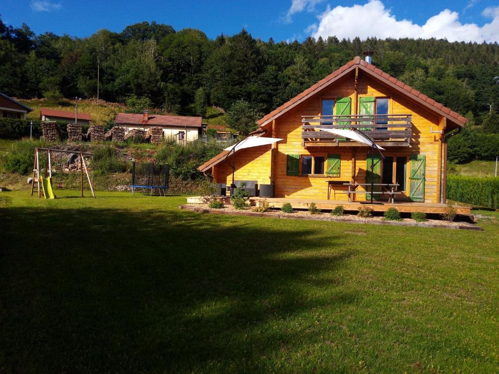 a wooden house with a playground in a field at Chalet des Brocards in Saint-Maurice-sur-Moselle