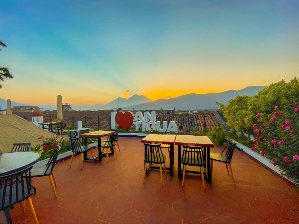 een groep tafels en stoelen op een patio met uitzicht op de zonsondergang bij El Carmen Hotel in Antigua Guatemala