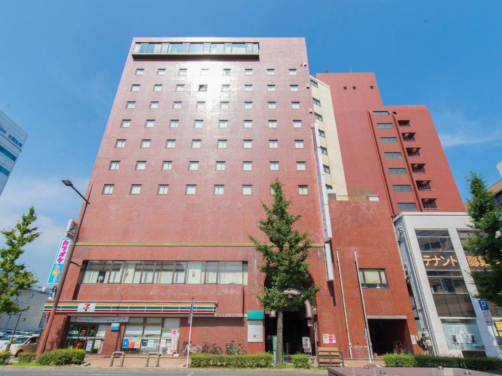 ein hohes rotes Backsteingebäude mit einem Baum davor in der Unterkunft Tabist Hotel Tetora Kitakyushu in Kitakyūshū