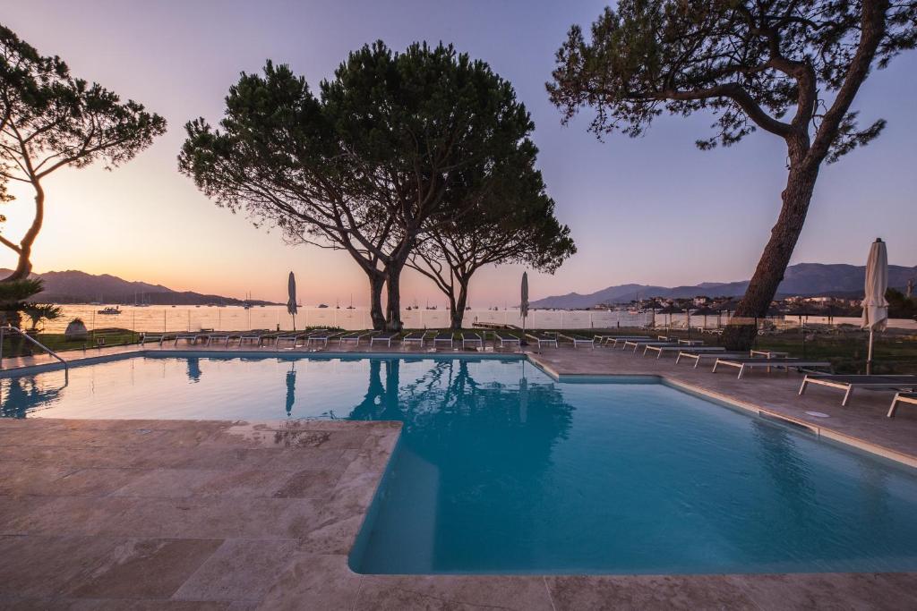 a swimming pool with trees and the ocean in the background at Hôtel La Roya in Saint-Florent