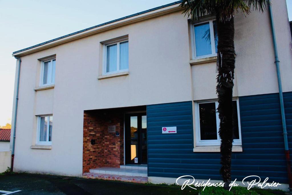 a white and blue building with a palm tree in front of it at Résidences du Palmier in Saint-Laurent-sur-Sèvre