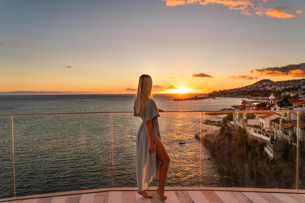 una donna in piedi su un balcone che guarda il tramonto di Okulus Madeira a Funchal