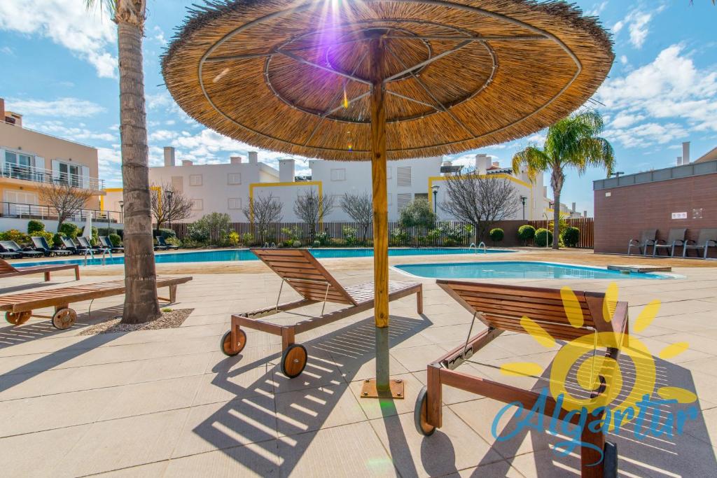 a pair of chairs under an umbrella next to a pool at Cabanas Gardens by Algartur in Cabanas de Tavira