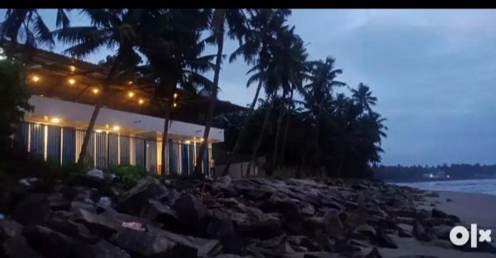 a building on a beach with rocks and palm trees at QUILON BEACH Inn in Kollam