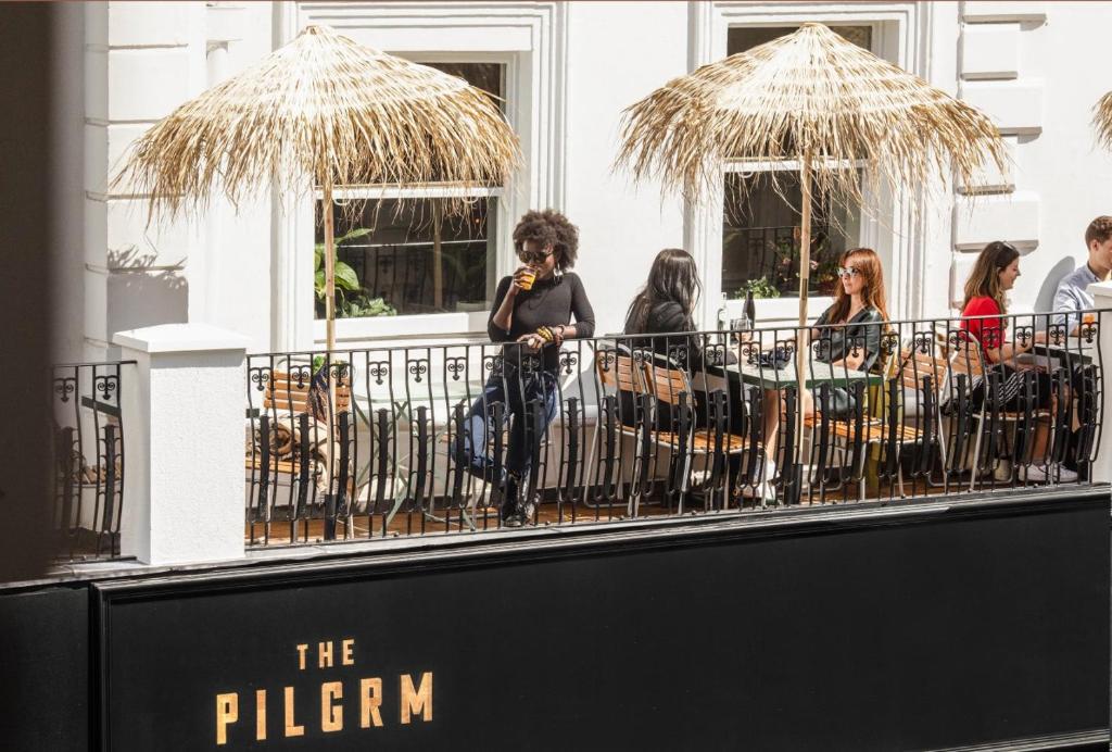 un groupe de personnes debout sur un balcon avec parasols dans l'établissement The Pilgrm, à Londres