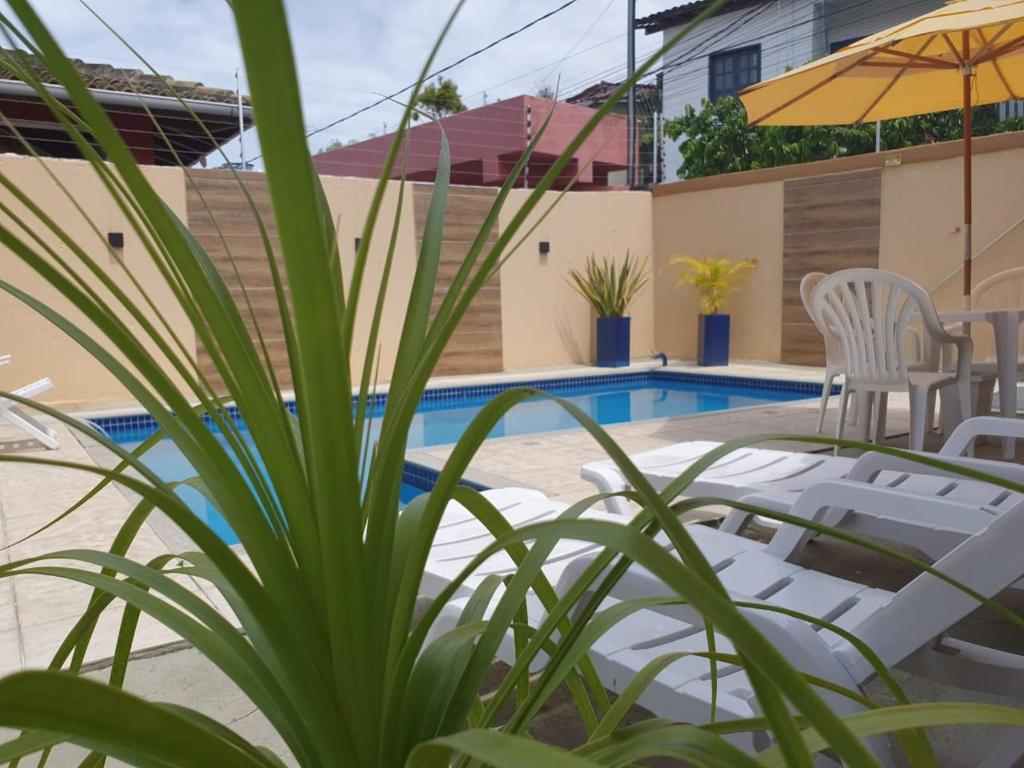 una piscina con sillas y una sombrilla junto a una casa en Pousada Cheiro de Cacau, en Arraial d'Ajuda