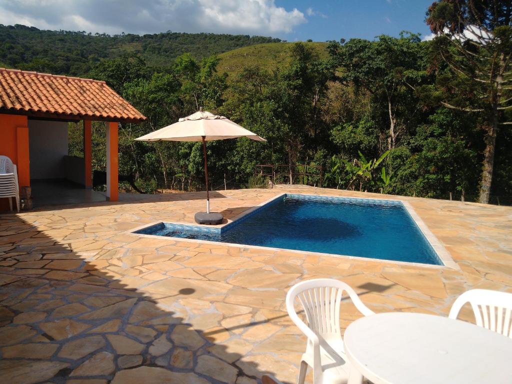 einen Pool mit Sonnenschirm, Tisch und Stühlen in der Unterkunft Sítio Pé da Serra - Pousada Rural in Capitólio