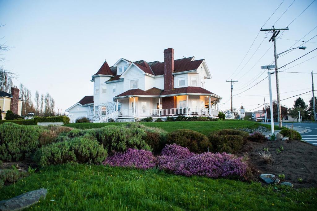 uma grande casa branca com um quintal com flores roxas em Anchorage Inn B&B em Coupeville