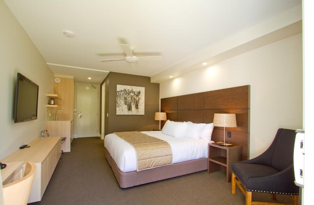 a hotel room with a bed, chair, desk and a television at The Remington Muswellbrook in Muswellbrook