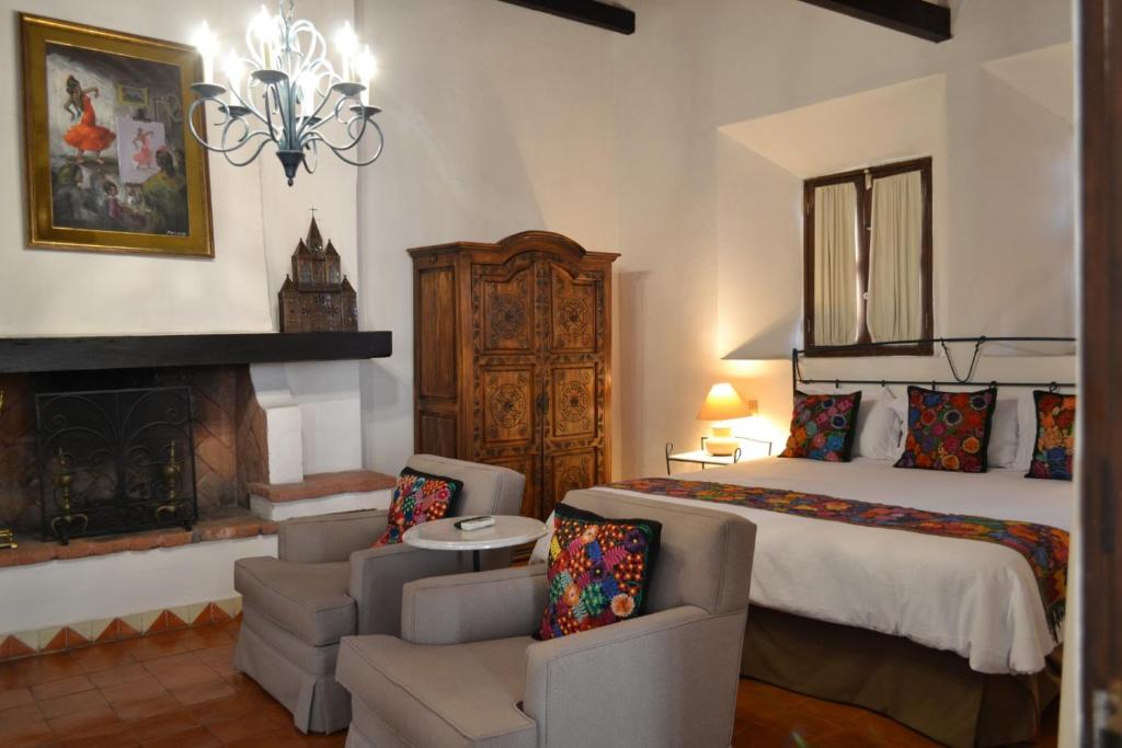 a bedroom with a bed and two chairs and a fireplace at Hotel Casa Rosada - Adults Only in San Miguel de Allende