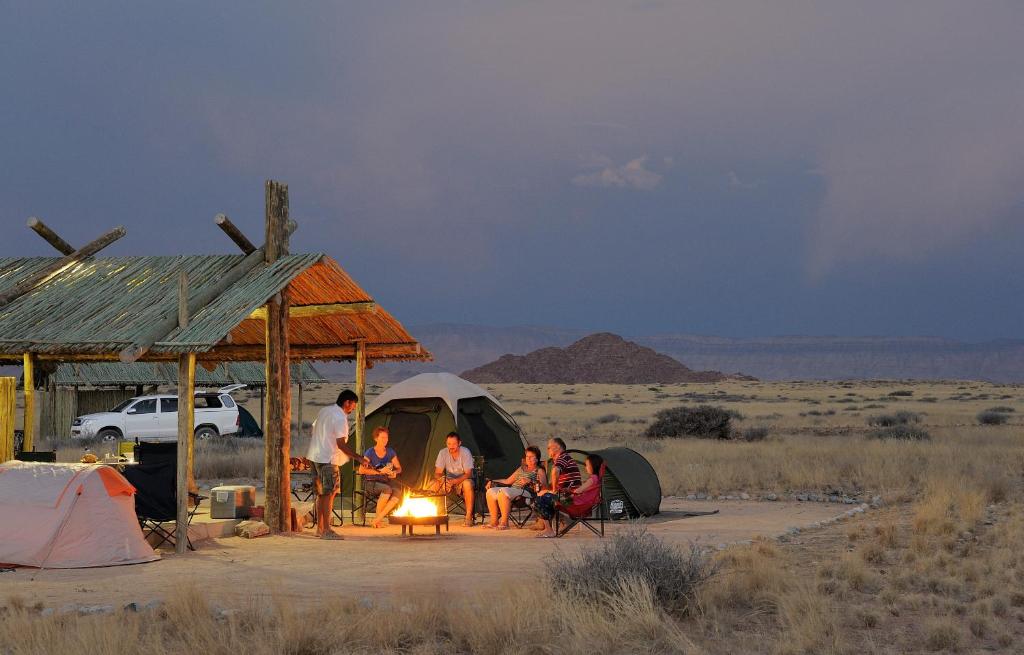 een groep mensen die rond een tent in de woestijn zitten bij Sossus Oasis Campsite in Sesriem