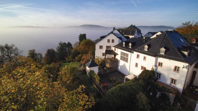 una gran casa blanca en una colina con niebla en el fondo en Burghaus & Villa Kronenburg, en Kronenburg