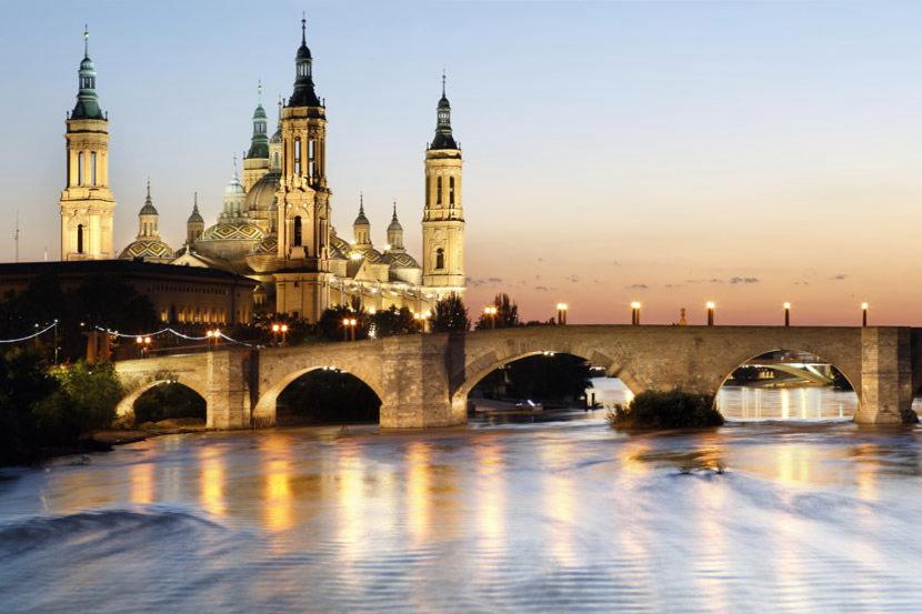 un puente sobre un río frente a un edificio en Zaragoza y sus 2 catedrales en Zaragoza