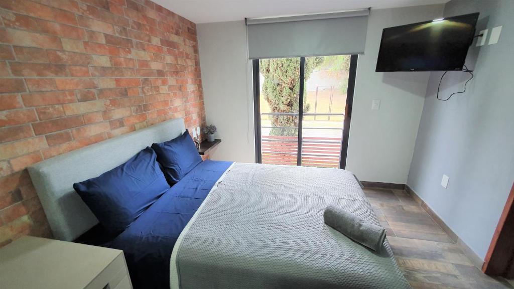 een slaapkamer met een bed met blauwe kussens en een bakstenen muur bij LUXURY STUDIOS AT CASONA 46 in Mexico-Stad