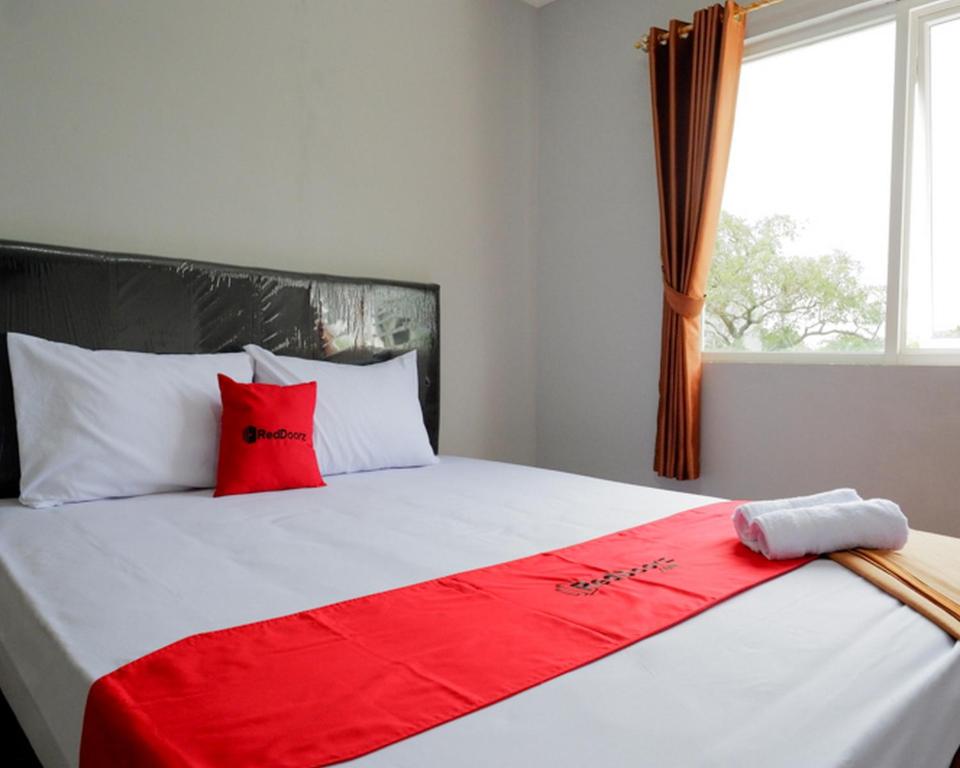 a bed with red and white pillows and a window at RedDoorz @ City Park Medoho Semarang in Alastuwo