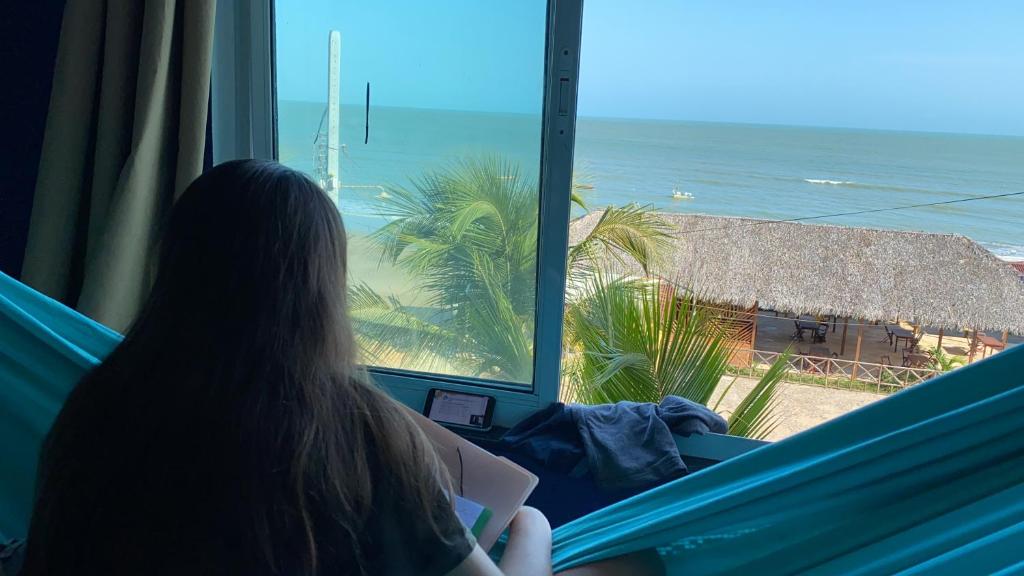 une femme assise dans un hamac et donnant sur une fenêtre donnant sur l'océan dans l'établissement Apartamento Vista Magnífica frente ao mar, à Luis Correia