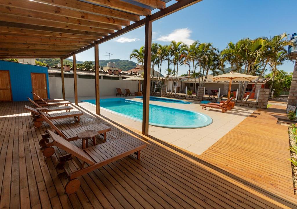 une terrasse en bois avec des bancs et une piscine dans l'établissement Pousada Nossa Senhora de Fatima, à Florianópolis