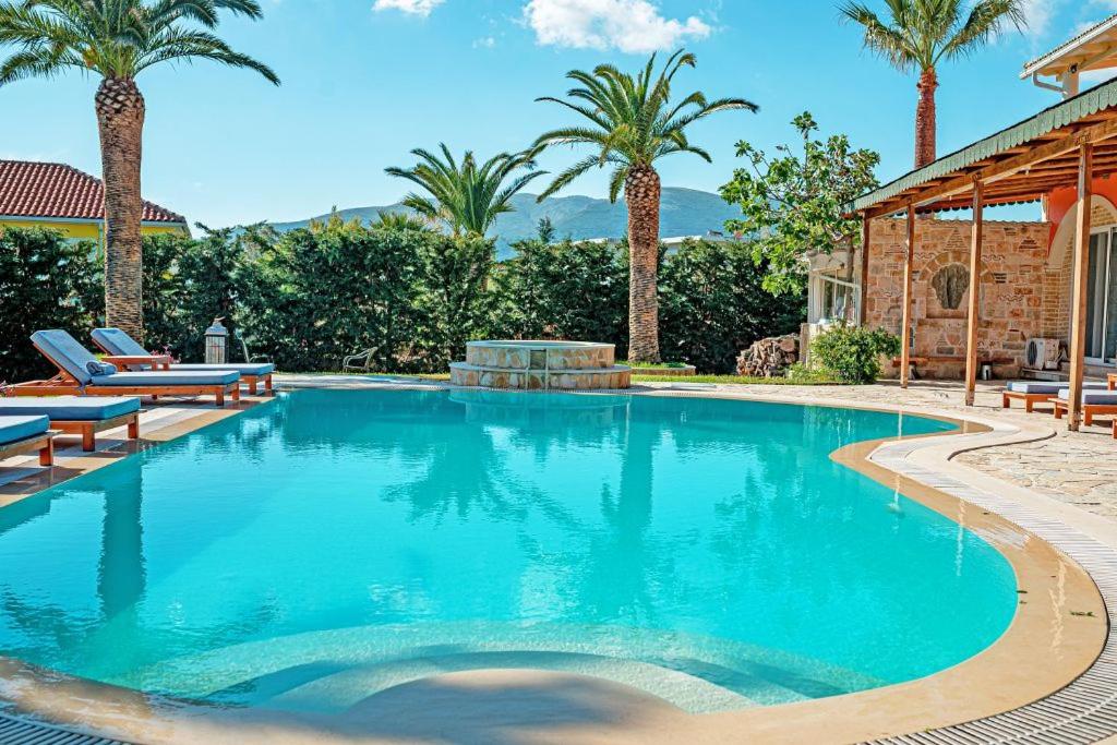 a swimming pool with palm trees and a house at Amor Villa in Laganas