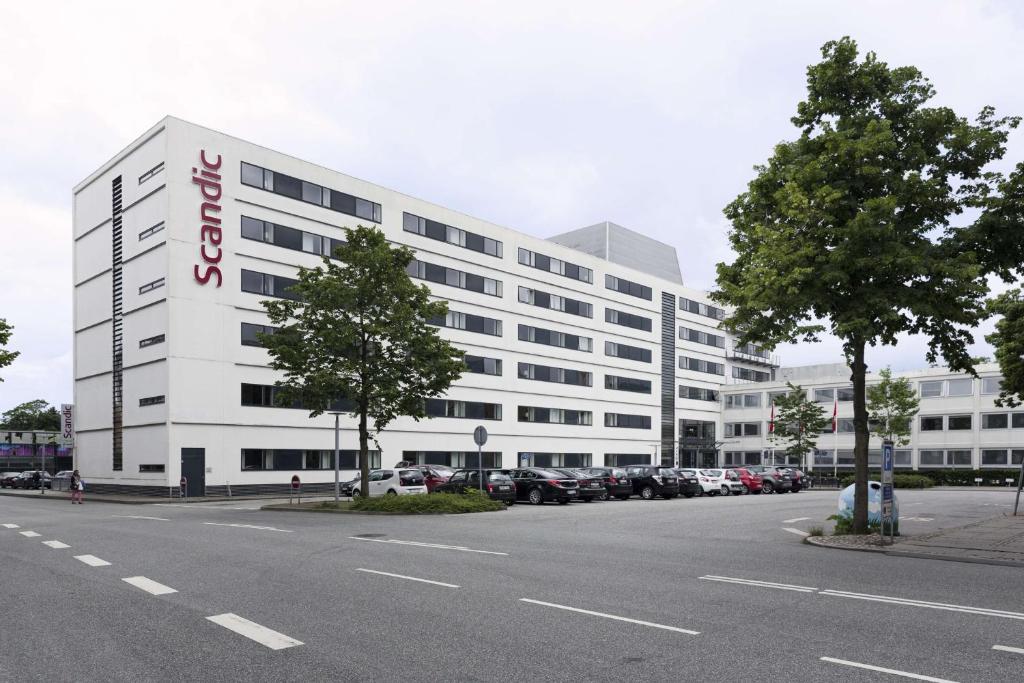 un gran edificio blanco con coches aparcados en un aparcamiento en Scandic Aalborg City en Aalborg