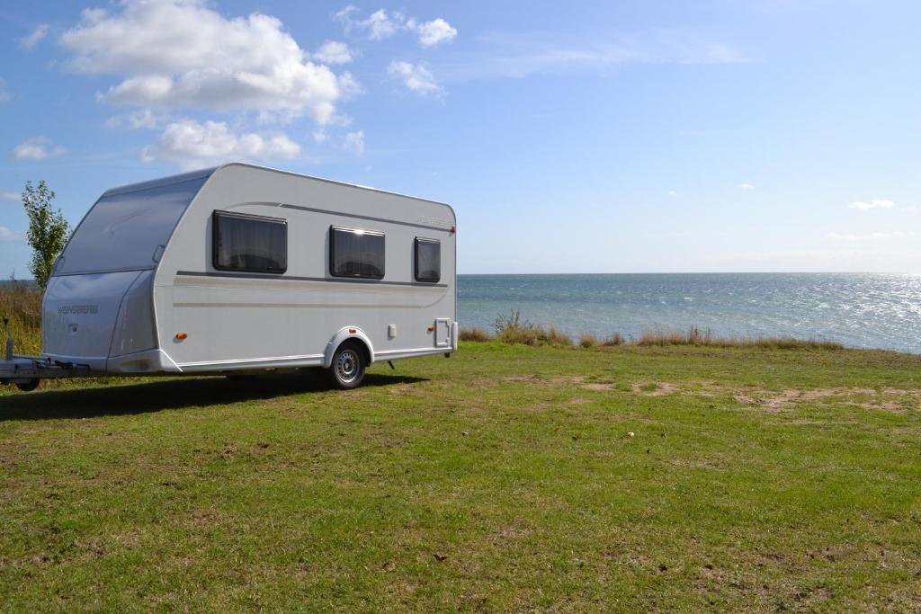 a caravan parked in a field next to the ocean at Mietwohnwagen Samson Fehmarn in Fehmarn