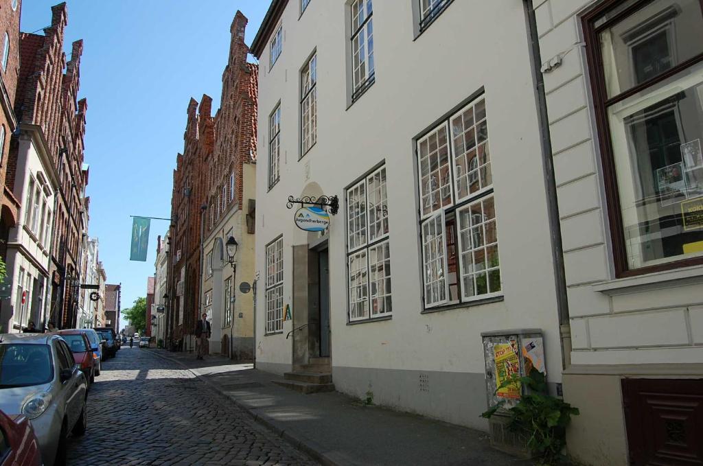 a street with buildings and cars parked on a cobblestone street at Jugendherberge Lübeck Altstadt in Lübeck