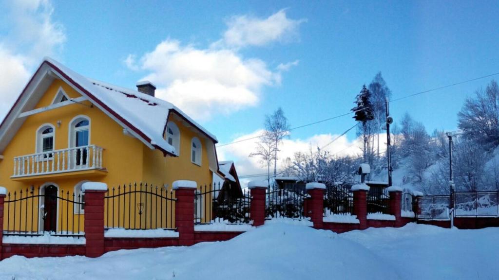 a yellow house with a fence in the snow at Penzion Dominika in Oravský Biely Potok