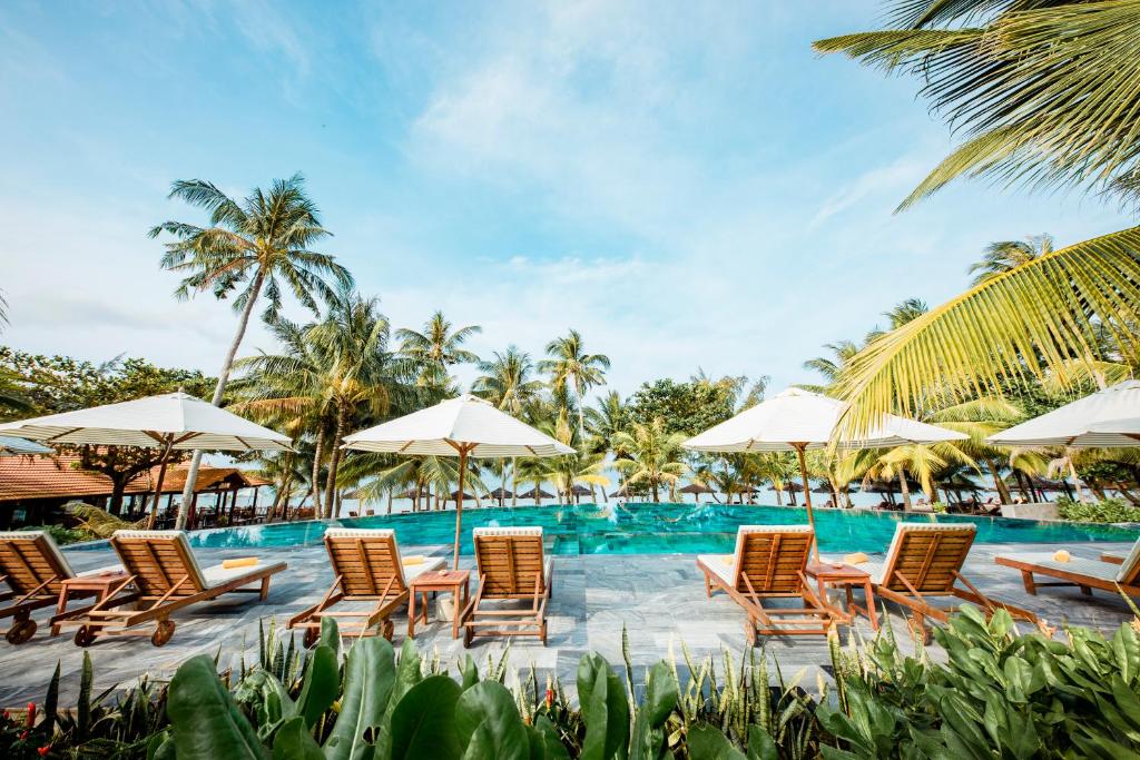 
a beach with a pool, chairs, tables and umbrellas at Thanh Kieu Beach Resort in Phú Quốc
