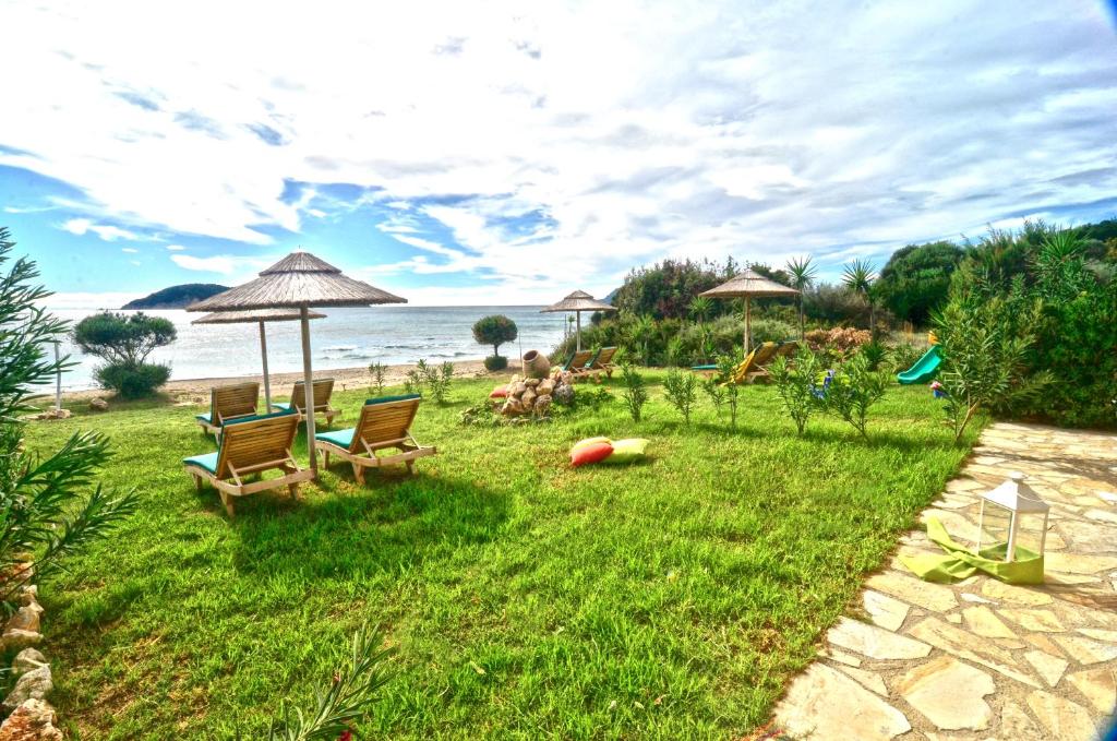 a lawn with chairs and umbrellas on the beach at Beachfront Elena Villa with mini pool and spa in Vasilikos