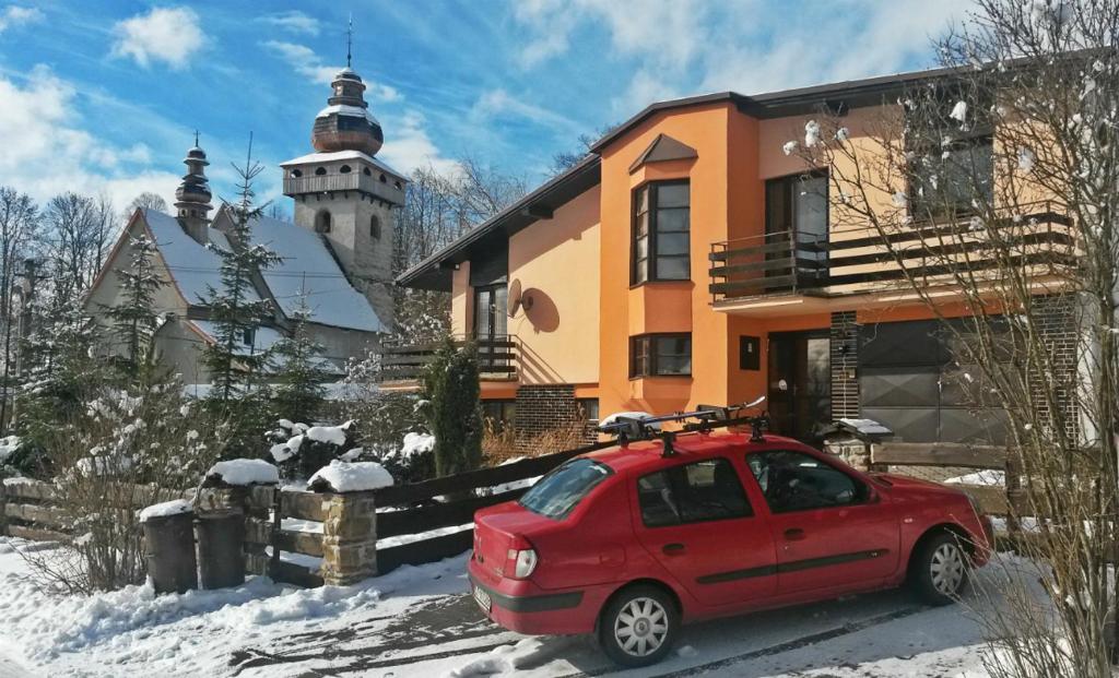 une voiture rouge garée devant une maison dans la neige dans l'établissement Rekreačný Dom Shalom, à Smrečany