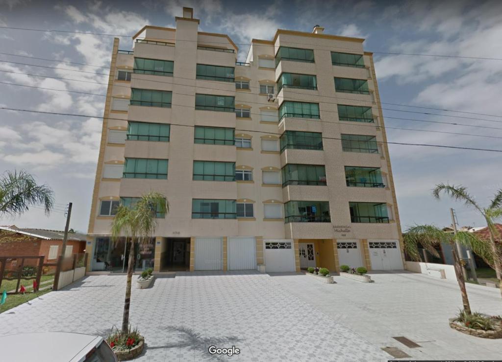 un gran edificio con palmeras delante en Aluguel Temporada Tramandai Proximo à Praia en Tramandaí