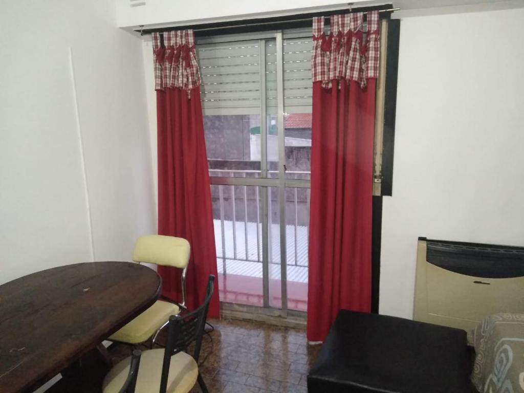 Habitación con mesa y ventana con cortinas rojas. en Residencia La Perla en Mar del Plata