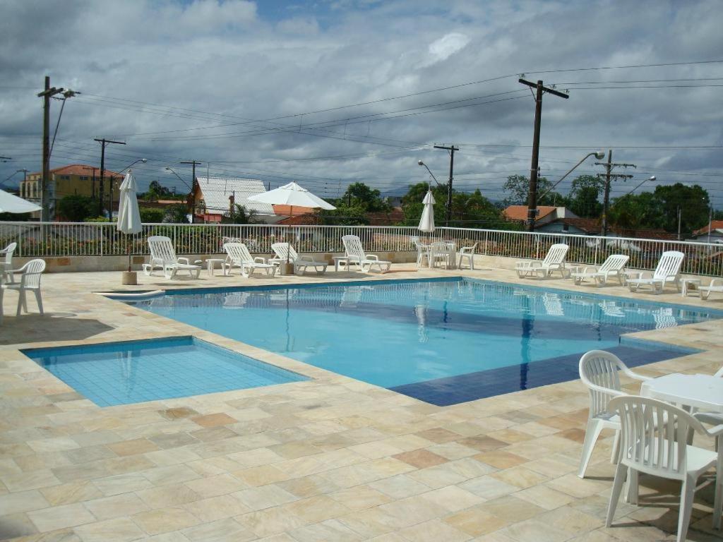 una piscina con sillas blancas, mesas y sillas en Golfinho Plaza Hotel en Cananéia