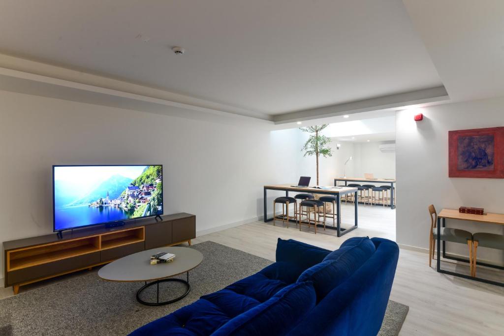 A modern apartment living room with a blue sofa, television and open dining-kitchen area.