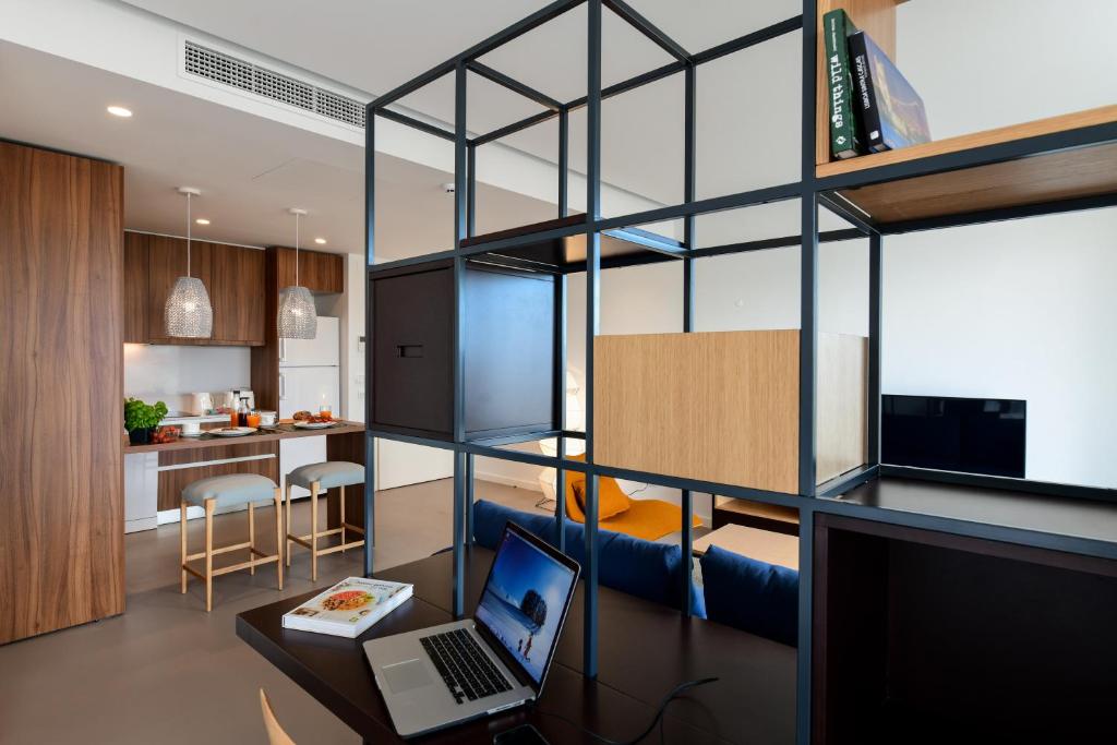 A desk beside a room-divider shelving unit, with the kitchen and television beyond.
