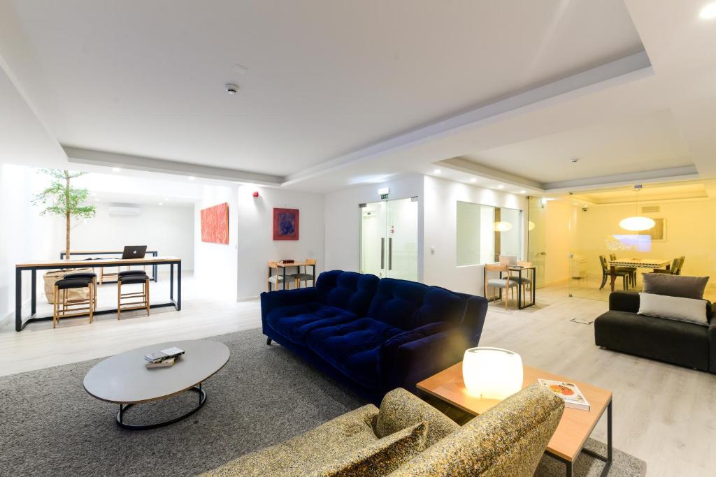 A spacious communal lounge with deep blue sofas, worktables, and a bright dining area.