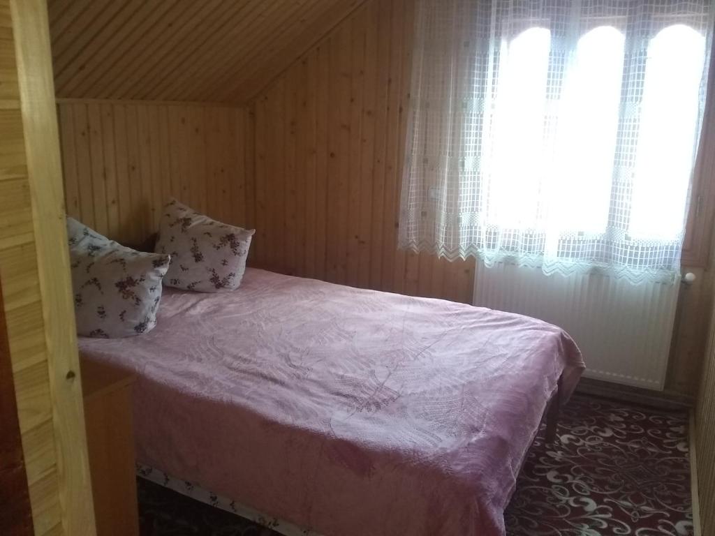a bedroom with a bed with pink sheets and a window at Хатина в горах in Yablunytsya